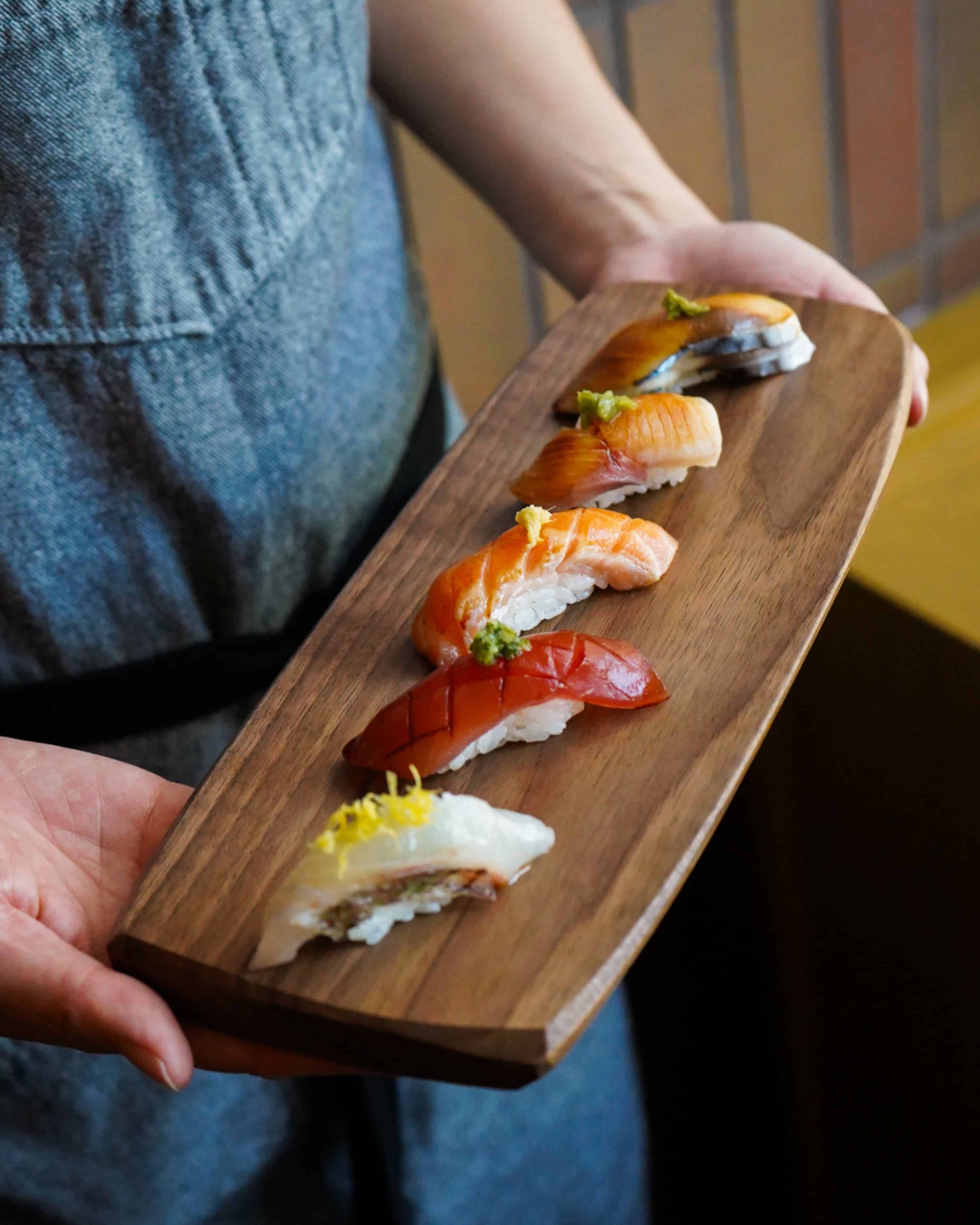 nigiri plated on a wood board being held by an uchiko chef