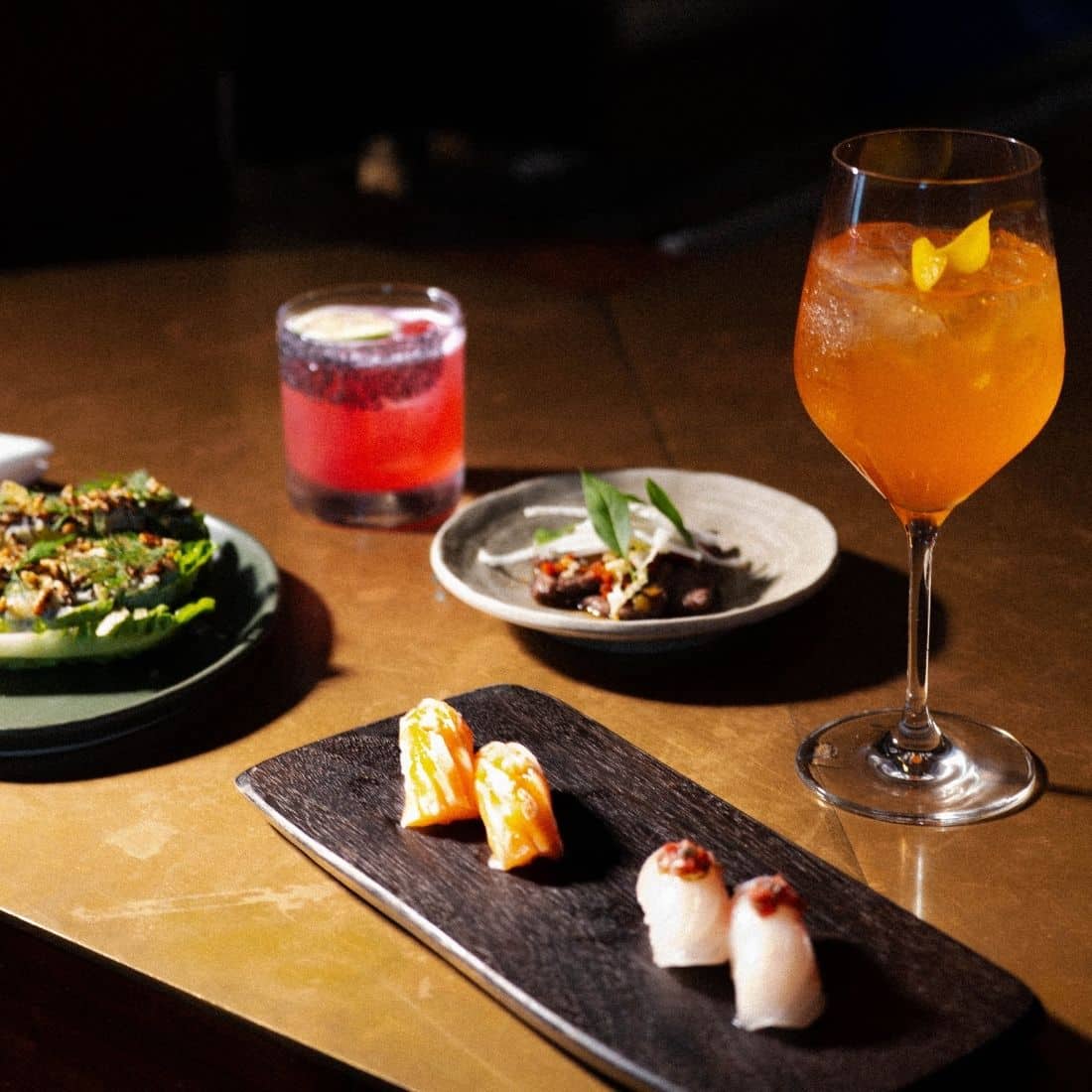 nigiri and salad plated in soft lighting with aperol spritz and a cocktail