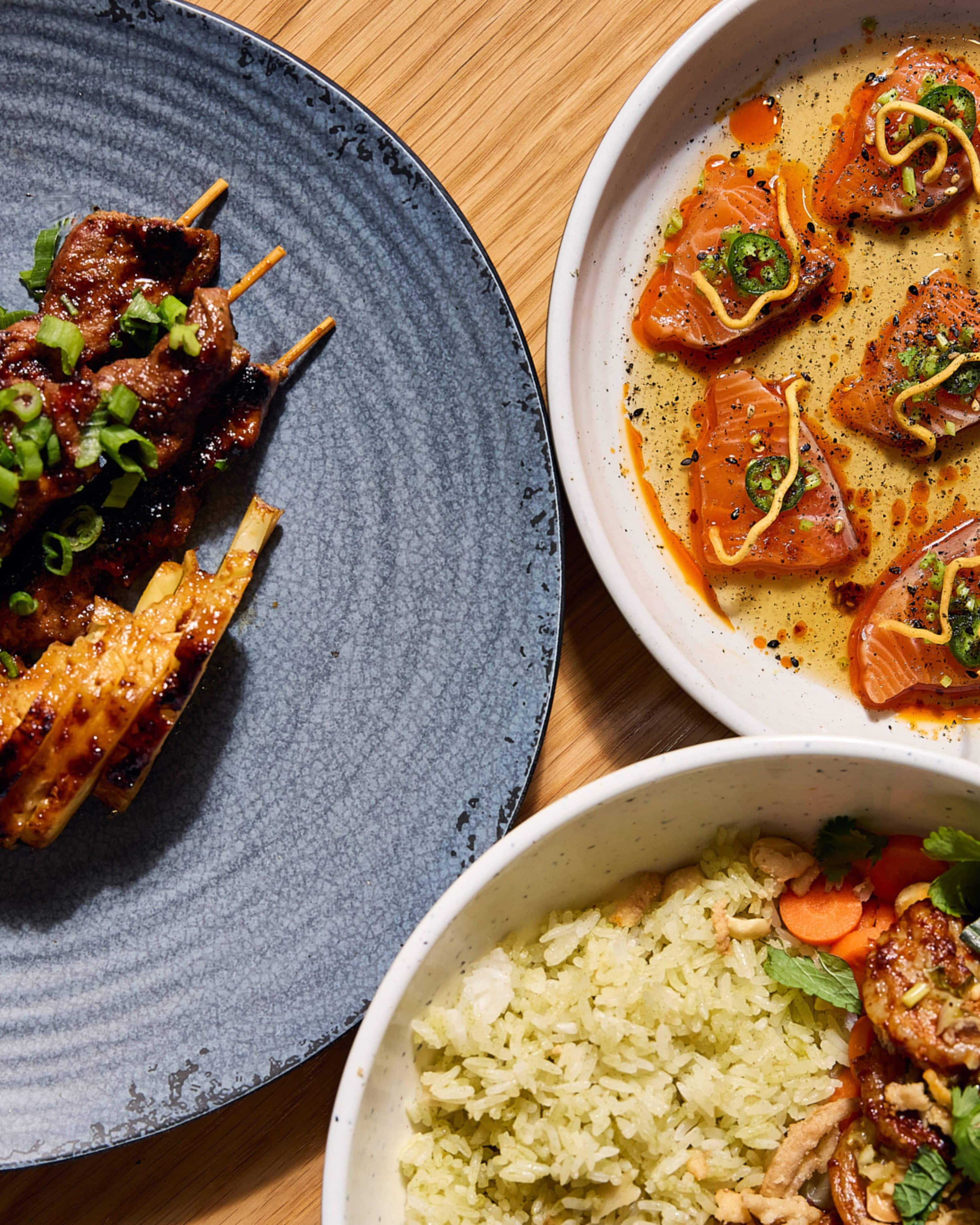 meat, rice, and crudo dishes on stoneware plates